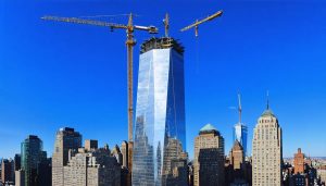 Aerial view of 2 World Trade Center under construction, featuring its stepped design and surrounded by symbols of global teamwork with various international flags.