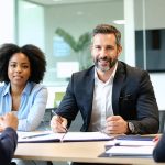 Professional property manager in business attire attentively listening and engaging with a diverse group of tenants in a modern office setting.