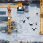 Aerial view of a construction site with advanced drones equipped with high-resolution cameras, LiDAR sensors, and thermal imaging systems actively monitoring cranes, scaffolding, and workers to enhance safety.