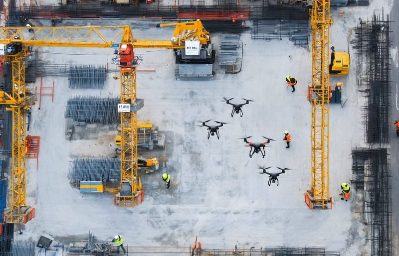 Aerial view of a construction site with advanced drones equipped with high-resolution cameras, LiDAR sensors, and thermal imaging systems actively monitoring cranes, scaffolding, and workers to enhance safety.