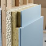 Layered wall insulation materials including closed-cell spray foam, rigid foam boards, and fiberglass batts arranged to represent an energy-efficient building assembly.