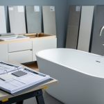 Modern bathroom fixtures and tile materials with contractor quote binders on a worktable, suggesting bathroom renovation scope and pricing comparison.